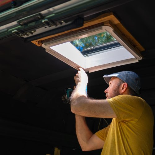Handyman using a cordless drill while installing a camper van roof window